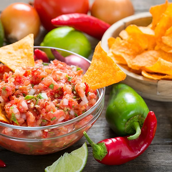 Fresh salsa with tortilla chips, surrounded by vibrant Mexican ingredients like peppers, onions, and lime.