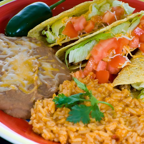 Los Amigos Mexican food plate with tacos, refried beans, rice, and a jalapeño.