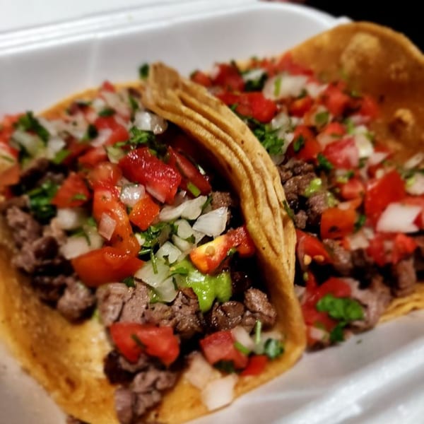 Two Los Amigos Mexican street tacos with carne asada, pico de gallo, and green sauce.