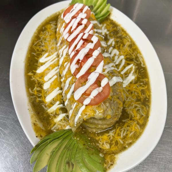 Los Amigos' burrito smothered in green sauce, cheese, sour cream, tomatoes, and avocado slices.